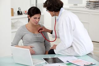 A doctor checks a pregnant woman's heart rate with a stethoscope.