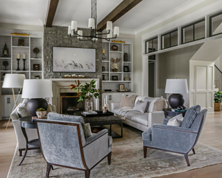 White living room with wooden ceiling beams, decorated with grey armchairs and with a cozy fireplace