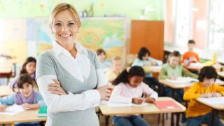 Smiling teacher stands in front of kids working at desks in classroom