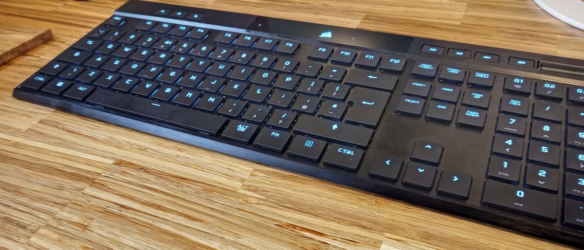 A black Corsair K100 Air Wireless keyboard on a wooden table