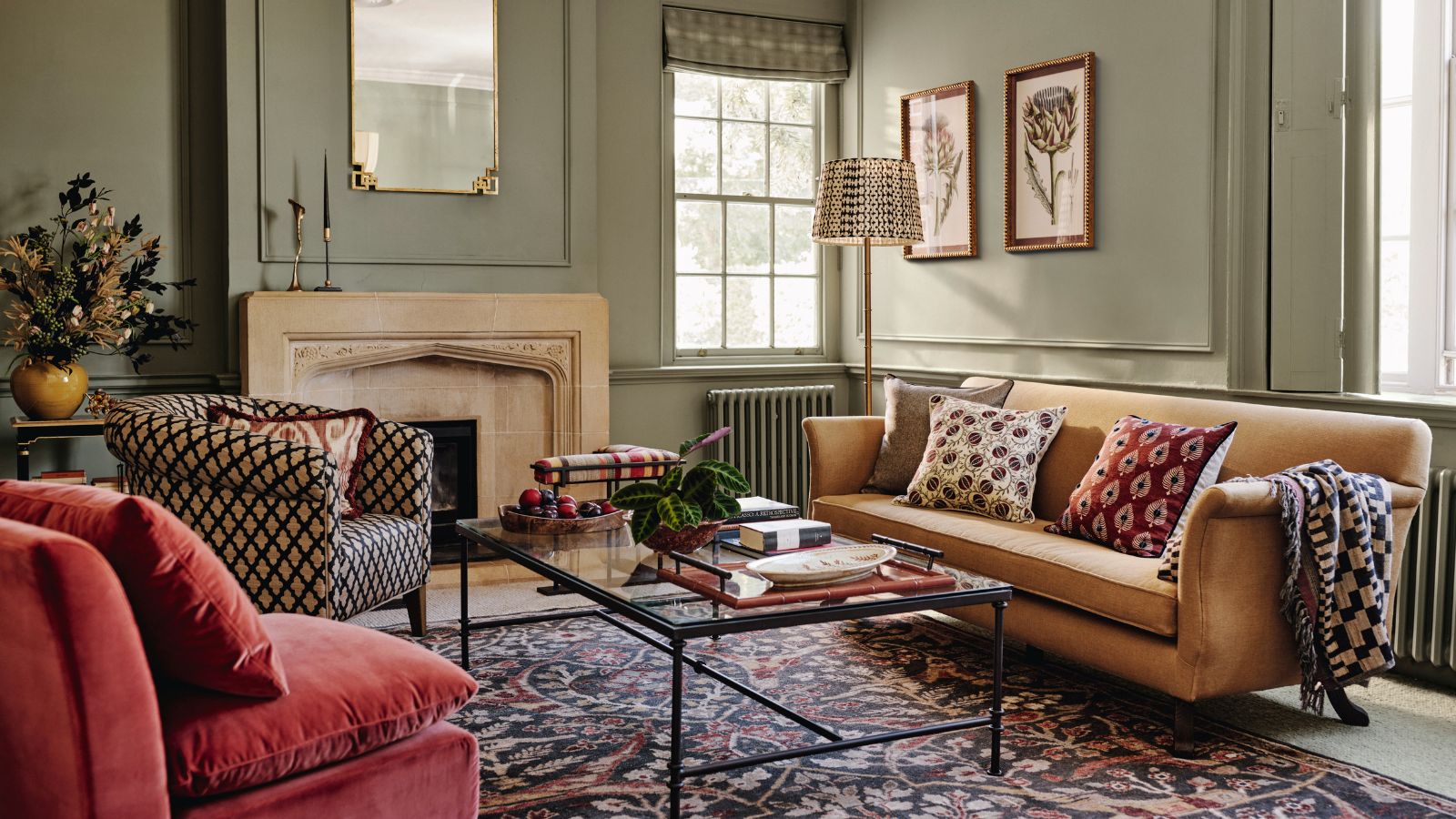 A green living room with a yellow sofa, red arm chair, and patterned arm chair around a glass coffee table, in front of a stone fireplace. 