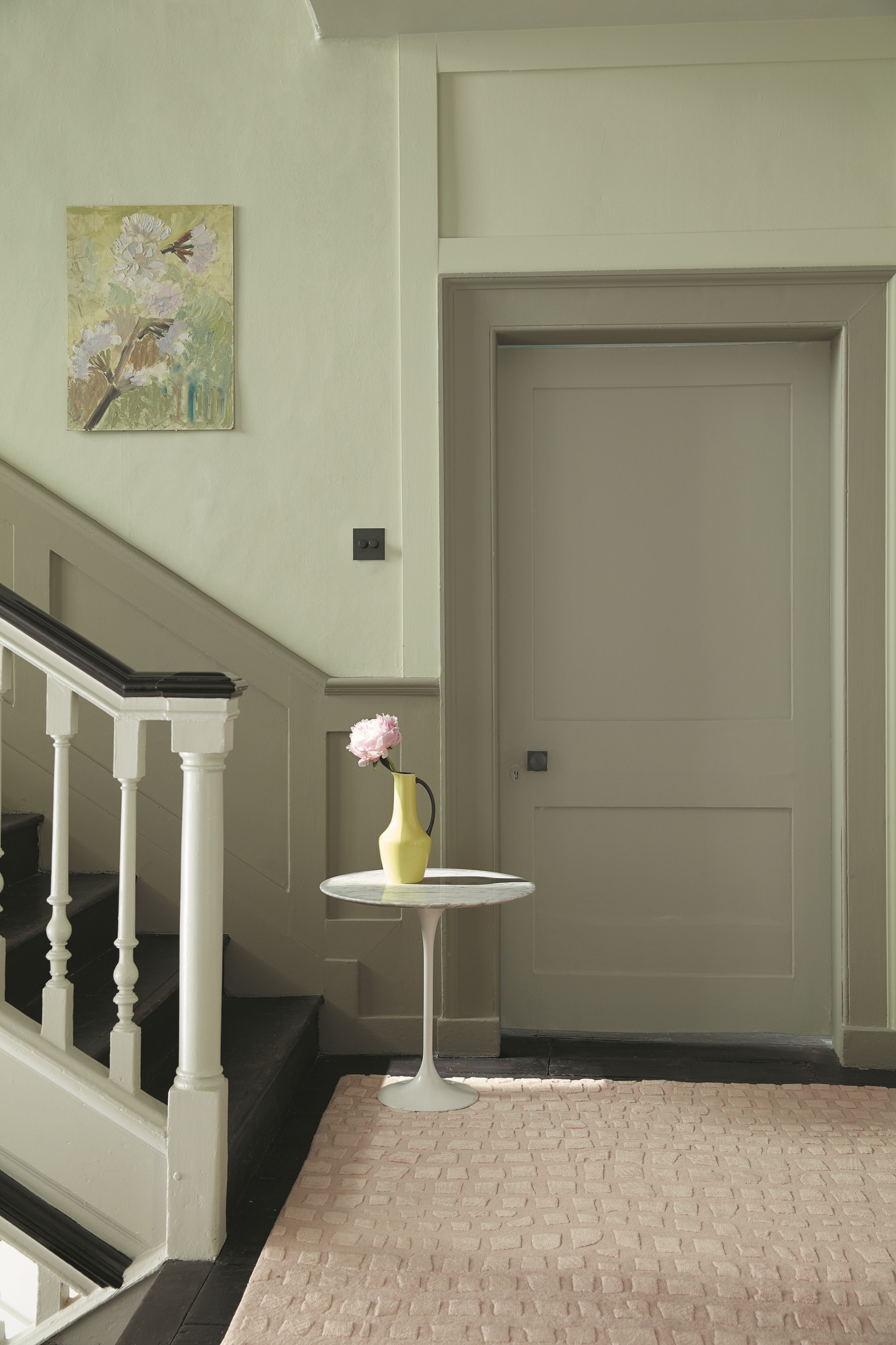 landing in victorian home with sage green walls, olive door, beige rug, side table with vase and flower, and artwork on the wall