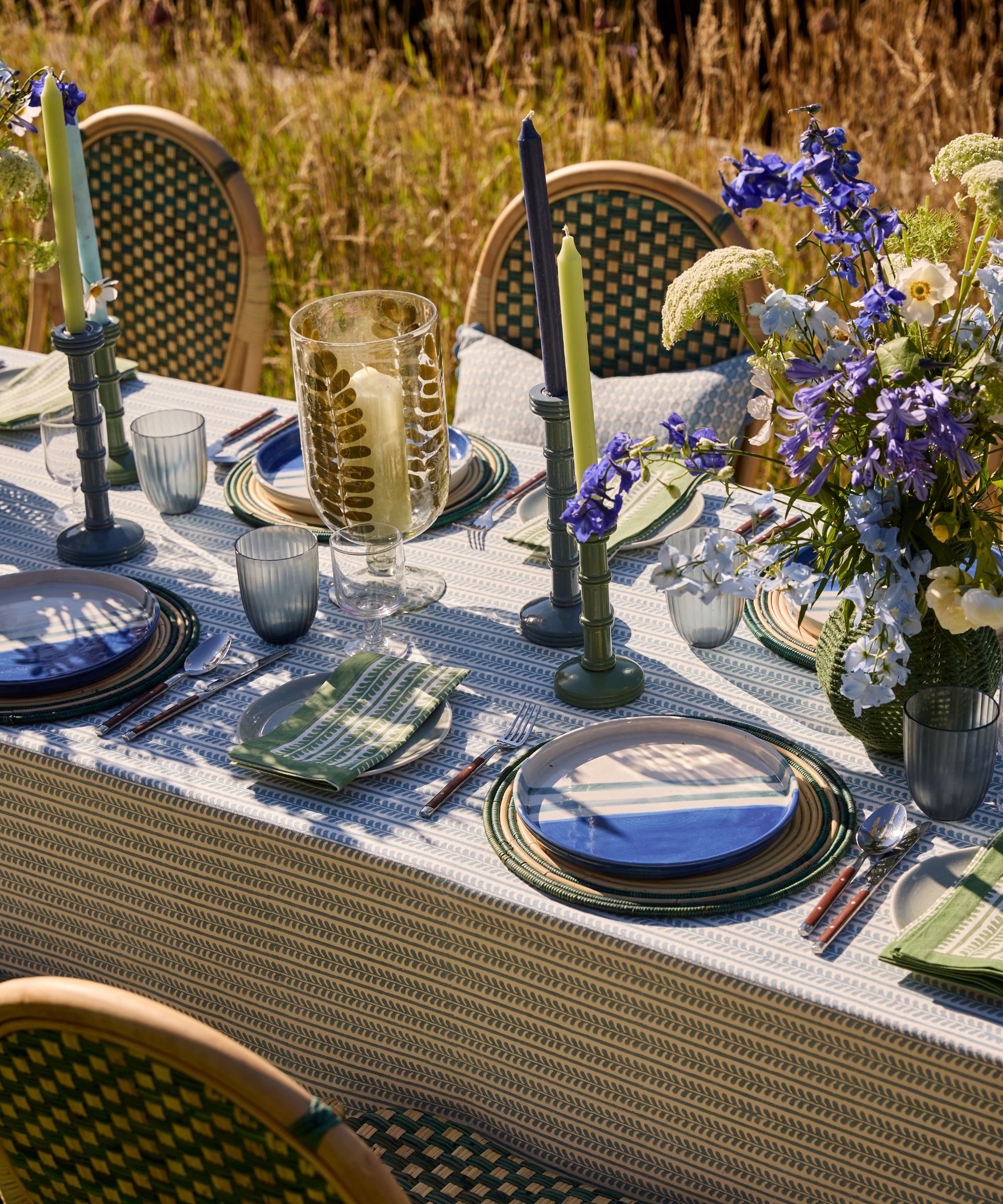 long outdoor table with rattan bistro chairs and a blue and green tablescape with large florals and tall taper candles