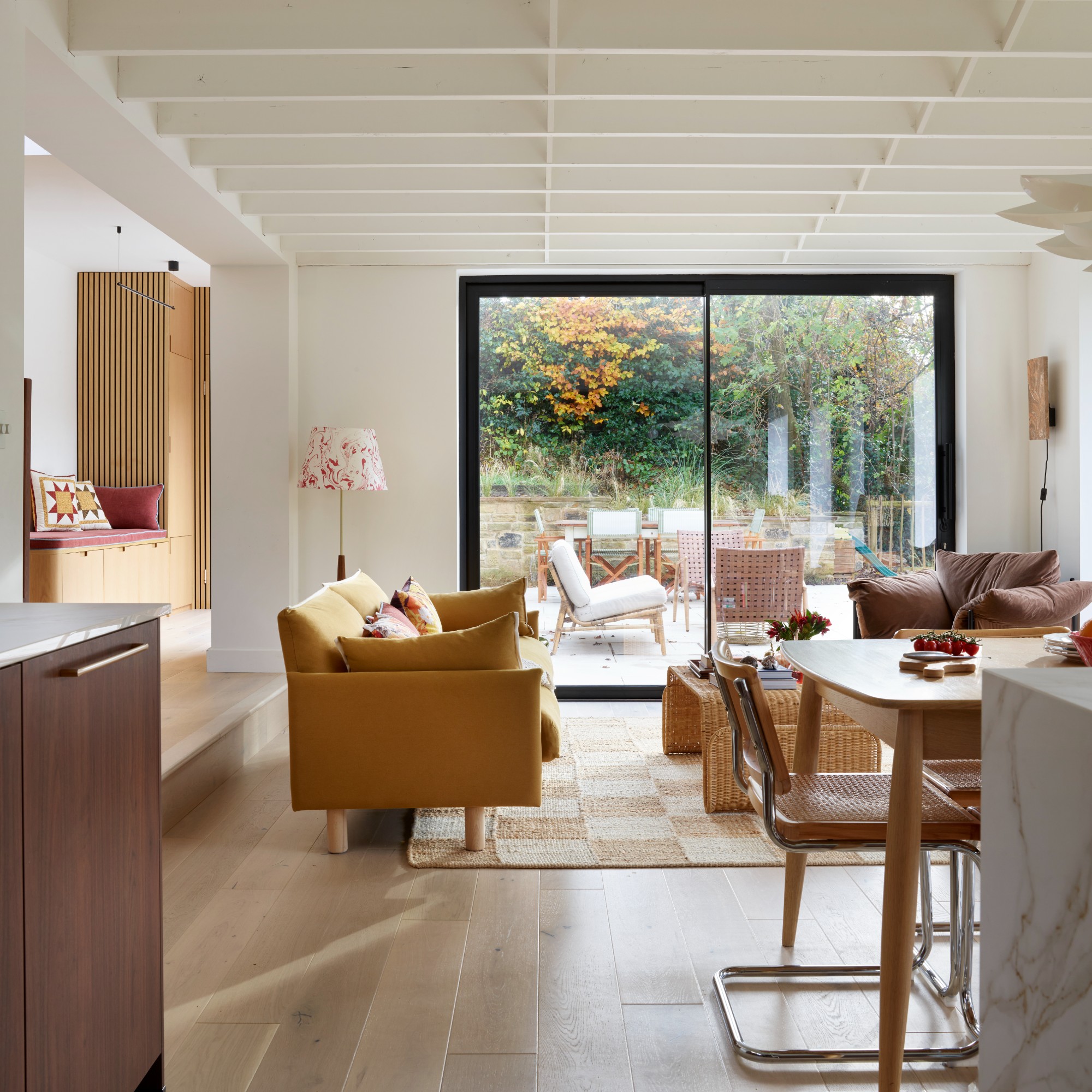 An open-plan living room with a yellow sofa and a chequered jute rug