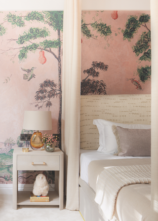 Pink botanical wallpaper set behind a cream, curtained bed.