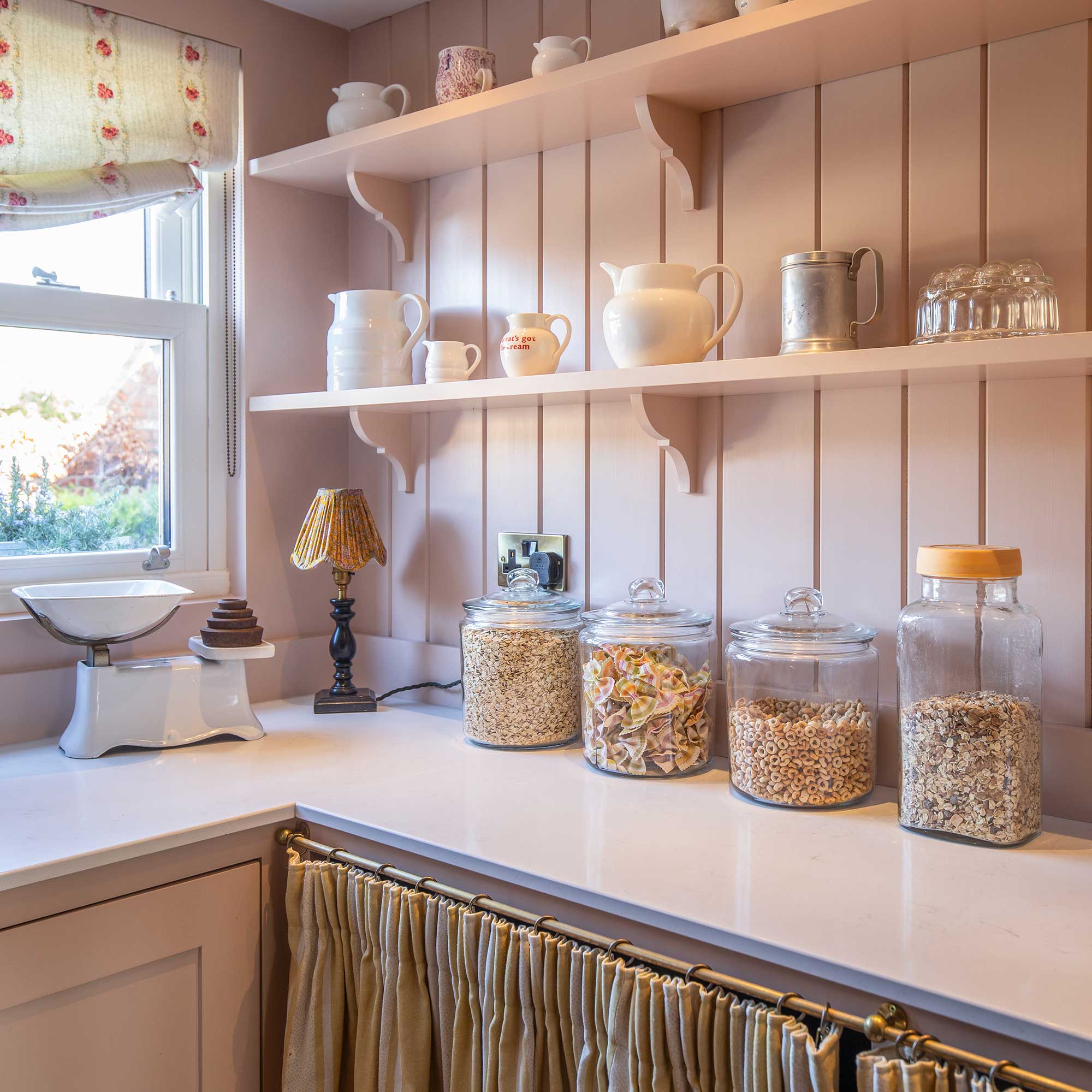 pink painted pantry with tongue and groove panelling, open shelves, cupboard skirts and white worktop