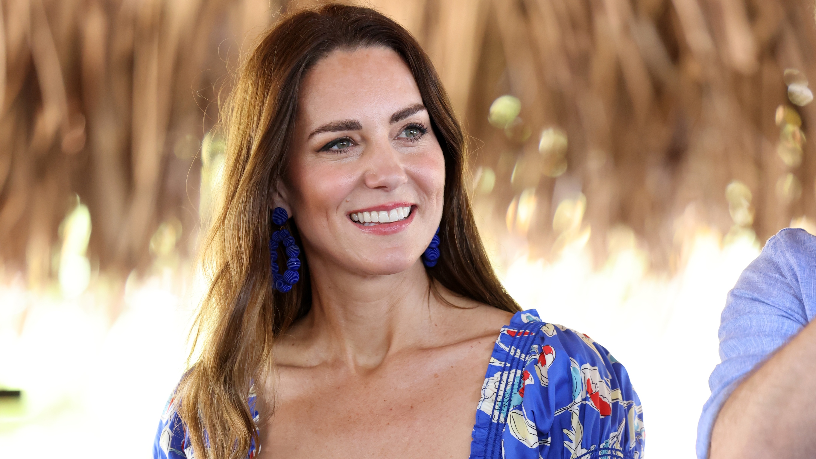 Catherine, Princess of Wales smiles during a visit to Hopkins in Belize, wearing blue statement earrings and a patterned dress