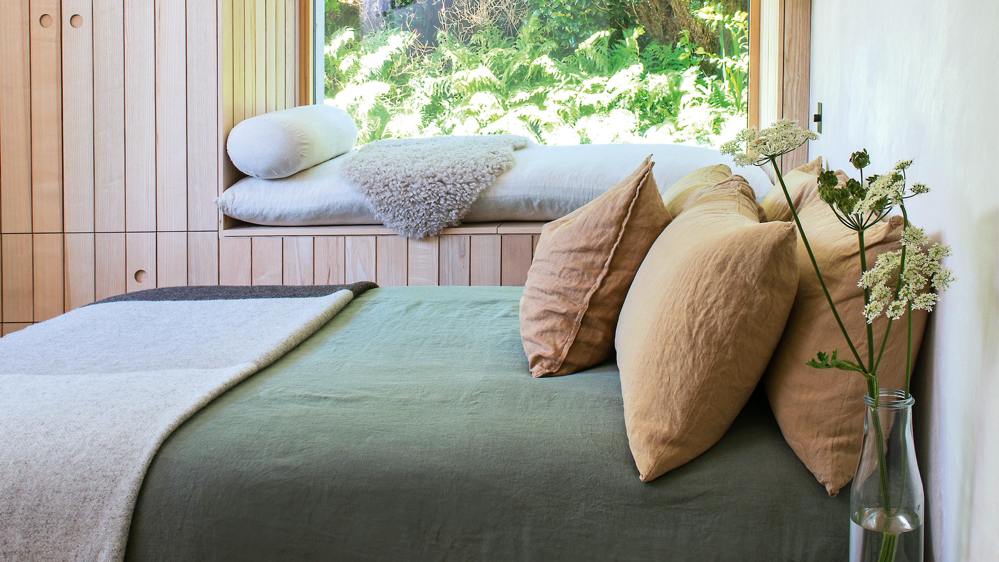 A wood panelled bedroom with a window seat and bed dressed in green and mustard coloured bedding