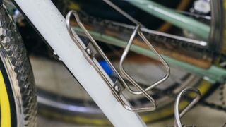 A stainless steel bottle cage on a white frame