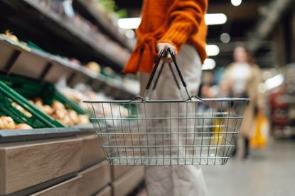 Lower section of young woman standing next to product aisle and choosing vegetables in the store. Young Asian woman doing grocery shopping in supermarket.