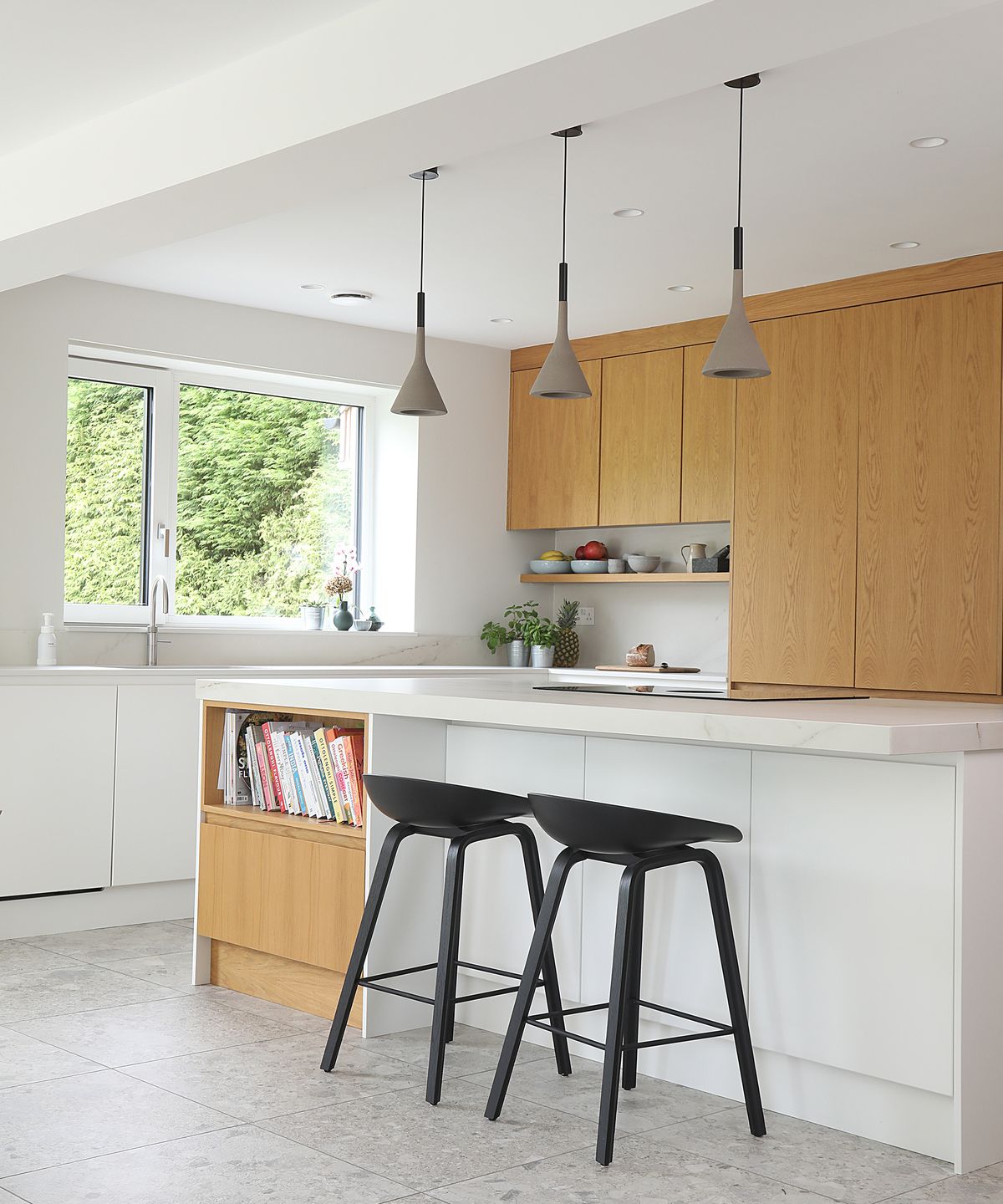 Kitchen island in a white kitchen with light wooden cabinet doors and grey pendant lights