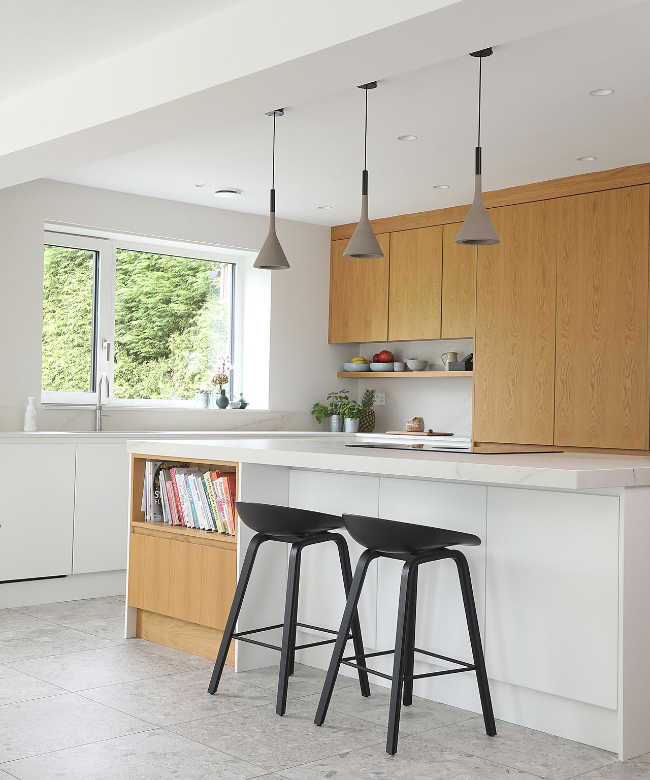 Kitchen island in a white kitchen with light wooden cabinet doors and grey pendant lights