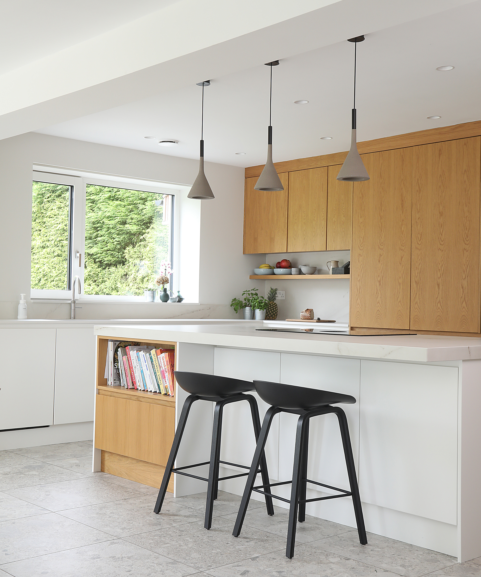 Kitchen island in a white kitchen with light wooden cabinet doors and grey pendant lights