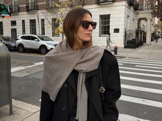 @jen_wonders on the streets of New York wearing a chic winter look with a black coat and a sweater worn as a scarf, styled with classic, elevated winter staples.