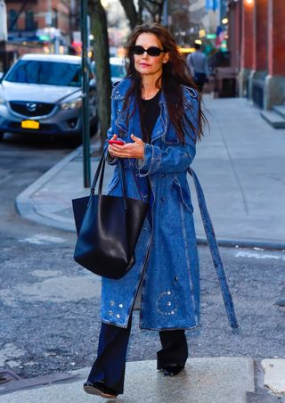 Katie Holmes walking in the street in a denim trench coat, dark-wash jeans, and a black tee.