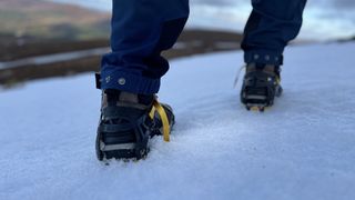 A pair of feet wearing Scarpa Mescalito TRK Pro GTX hiking boots in snow, walking away from the camera.