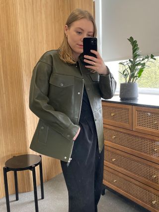 Woman in mirror wears green leather jacket and black trousers