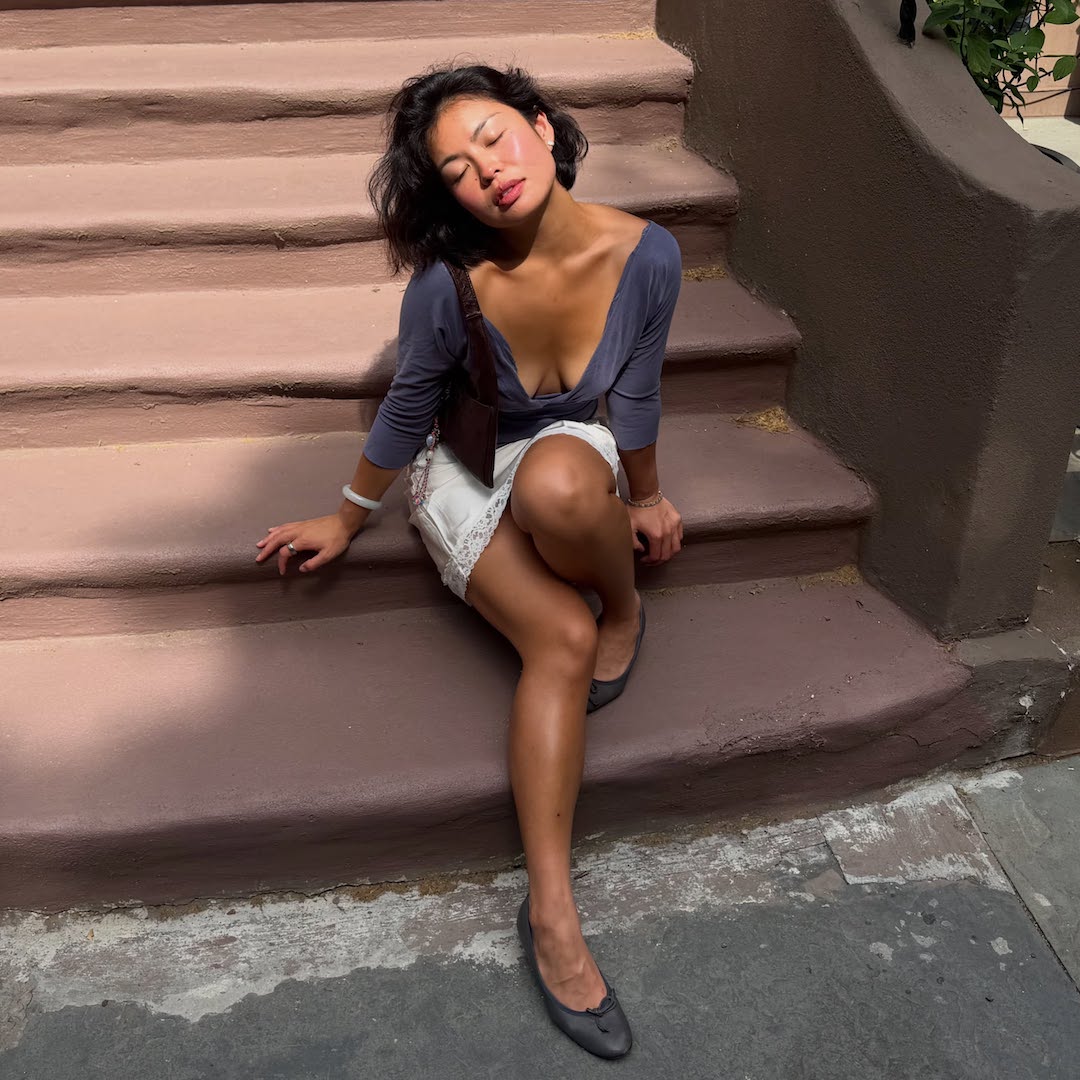 Allison Ho sitting on steps in lace dress, ballet pumps and glowy skin