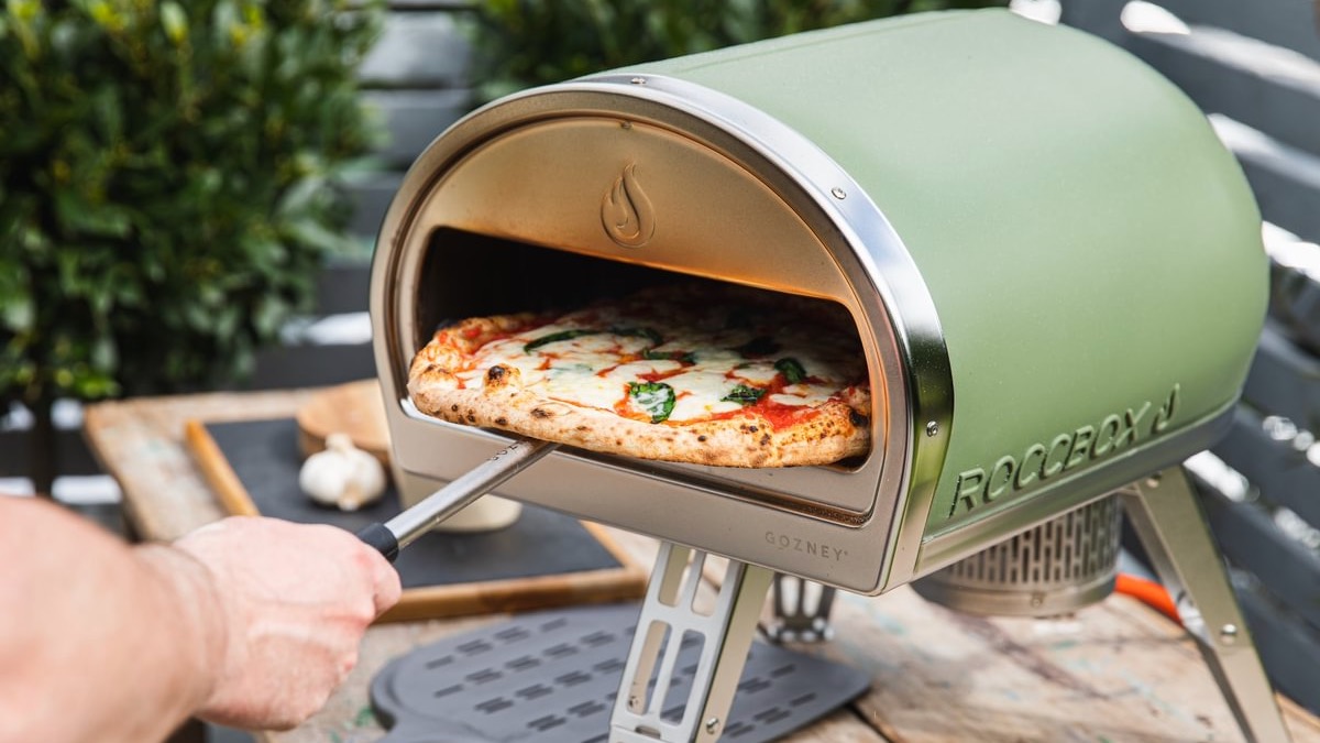 A person removing a cooked pizza from the Gozney Roccbox in Olive colourway