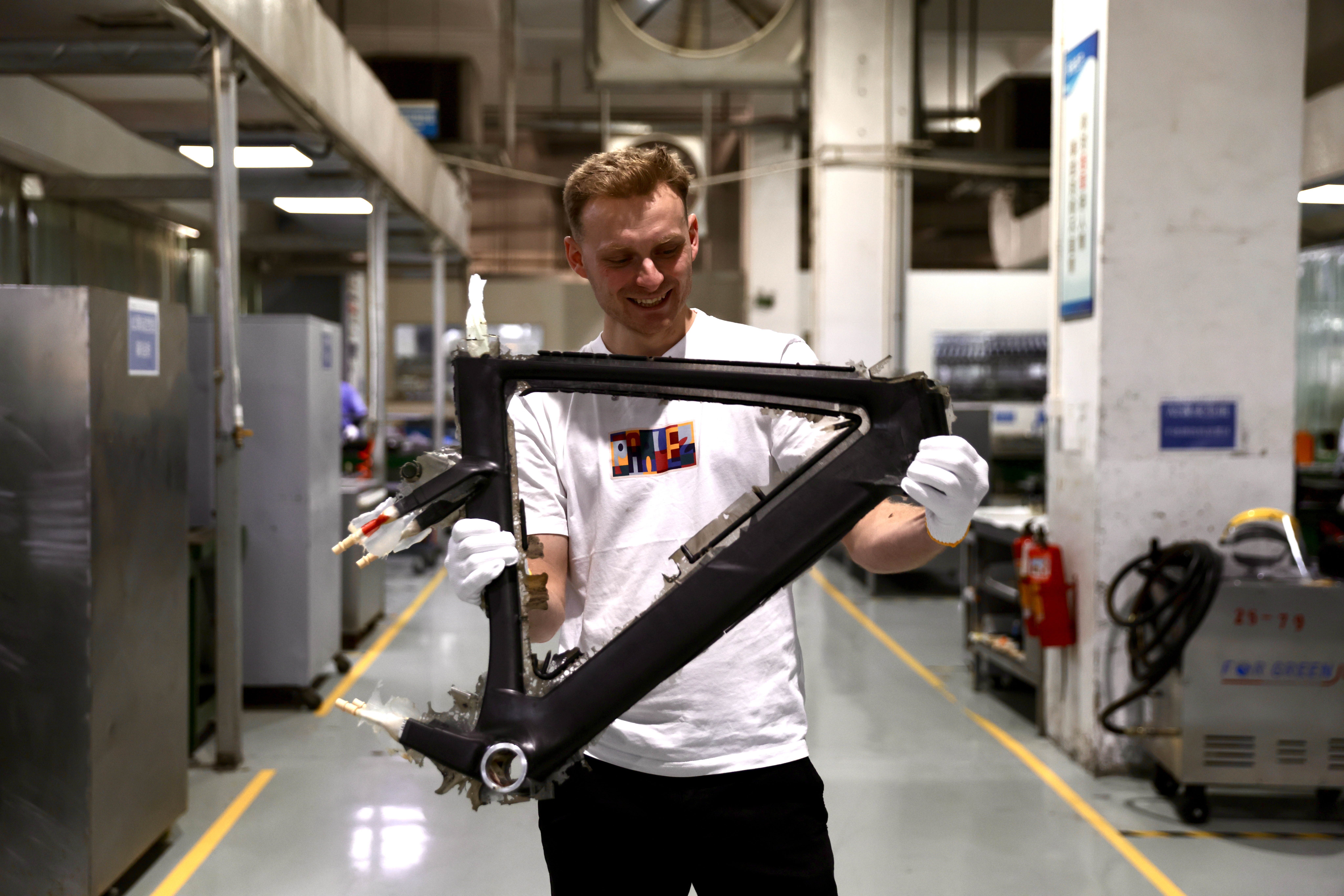 Jamie Williams in a white T-shirt holding a bare carbon bike frame in a factory