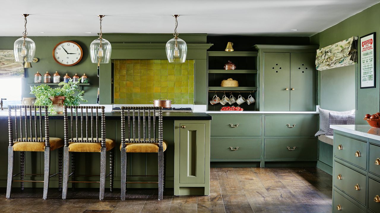 green kitchen with clear pendant lights, wooden flooring and mustard island stools 