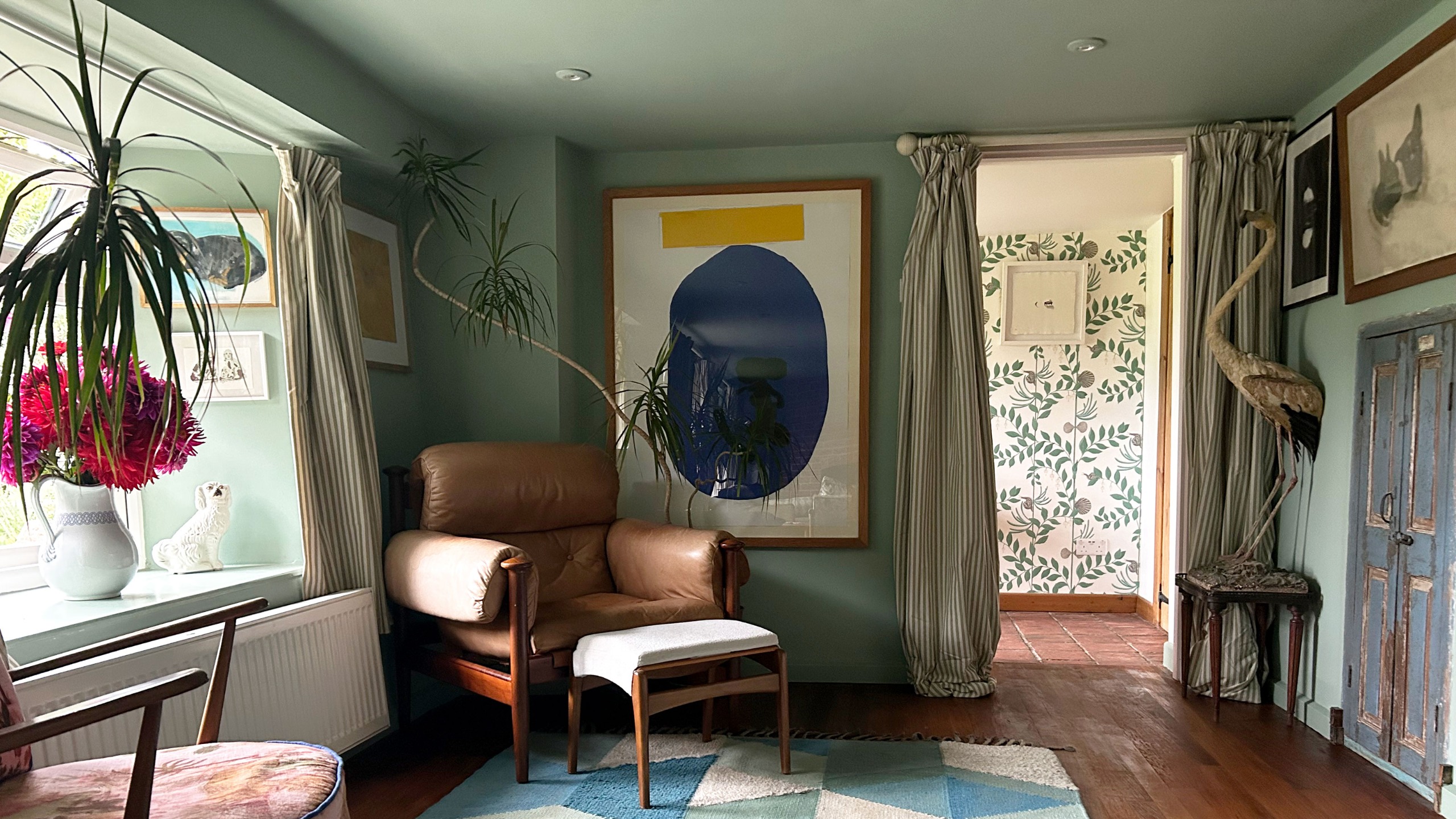 Living room with walls and ceiling painted green, wooden floor, artworks on walls