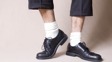 A man's bare legs show between the hems of his trousers and the tops of his white socks and block shoes.