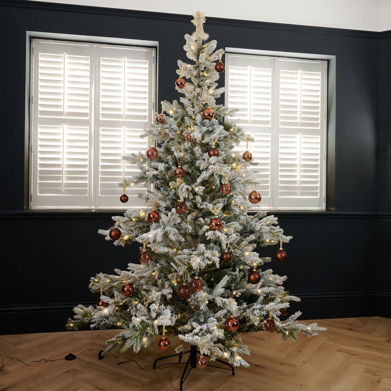 Cox &amp; Cox's Snowy Bergen Spruce Pre-Lit Christmas Tree decorated with brown baubles set up in a black-painted living room