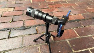 A high-angle shot of the Apexel 36X Telephoto Lens attached to an iPhone 16 plus and mounted on a mini tripod.