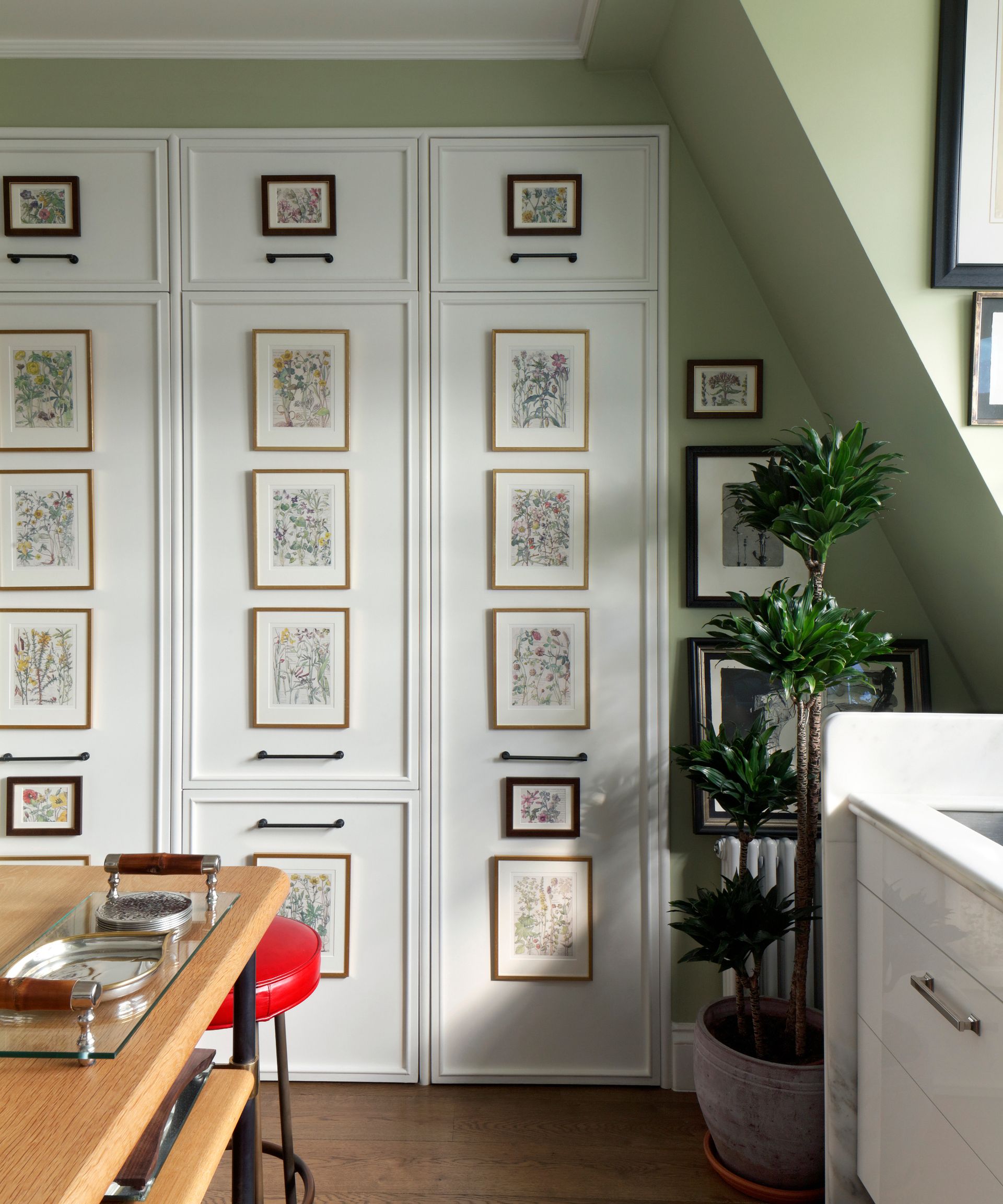 green painted kitchen with wooden table and panelled storage doors with artworks on
