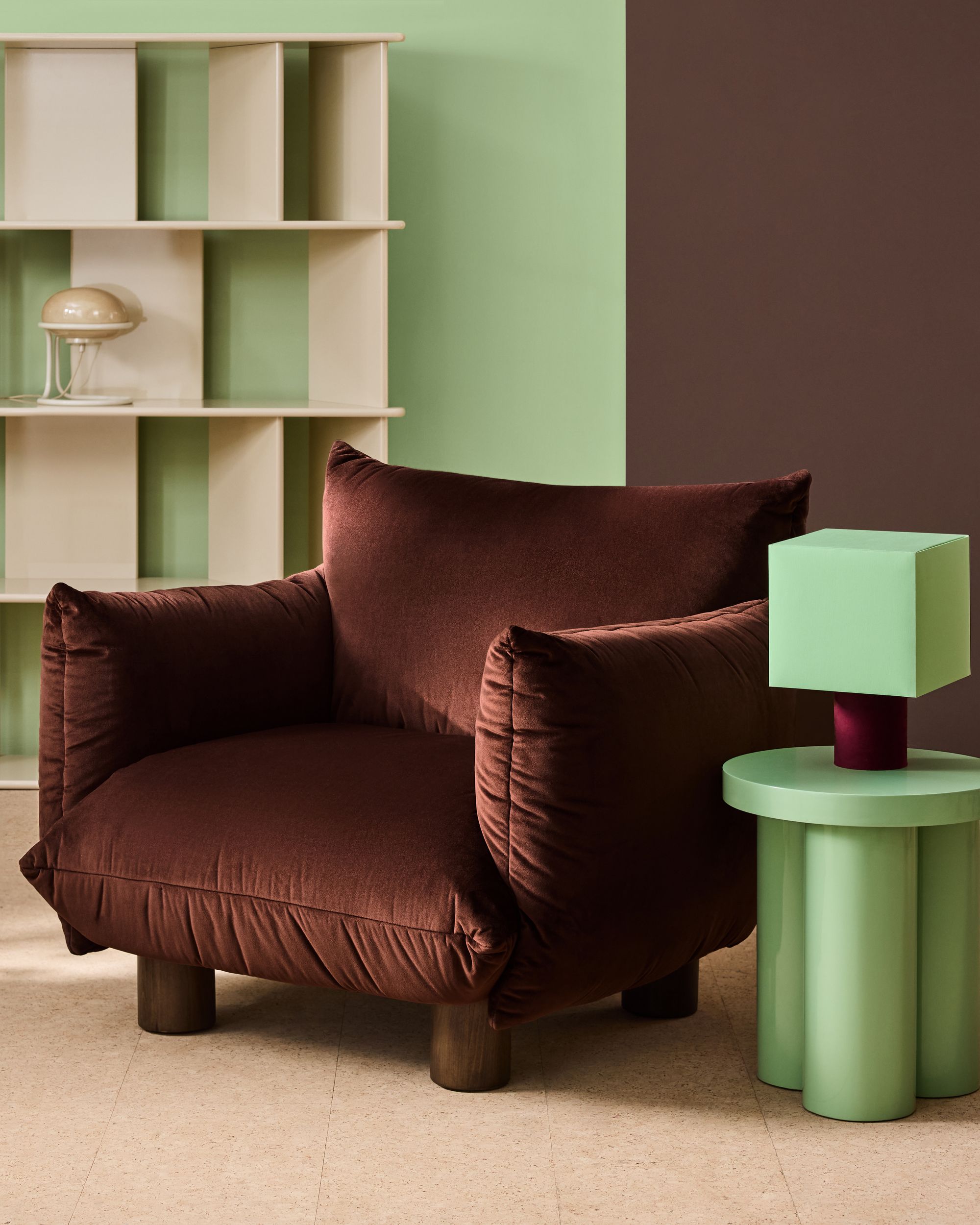 Image of a dark brown velvet accent chair with a mint green side table next to it. There is a mint green and burgundy lamp on the table and the wall are painted in mint green and brown.