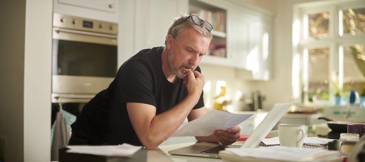 A man in a kitchen examining his payslip reviewing salary sacrifice for his pension