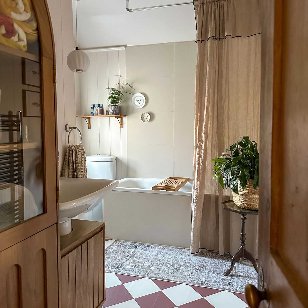 Small bathroom with chequerboard tiled floor, linen-look shower curtain, wall panelling and built-in bath