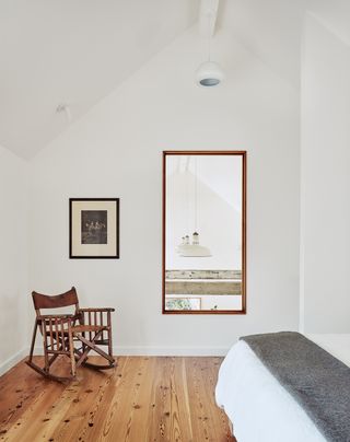 Bedroom with wooden floors, a rocking chair and a mirror on the wall