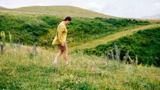 woman in shorts and shirt walks down a hill in the countryside