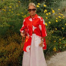 A women at Copenhagen Fashion Week in a red and white button-down shirt and white skirt in front of grass