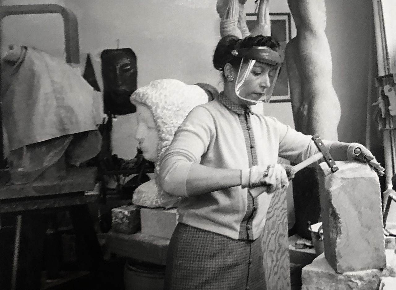 Naomi Feinberg in her workshop, holding a sculpting tool on a brick