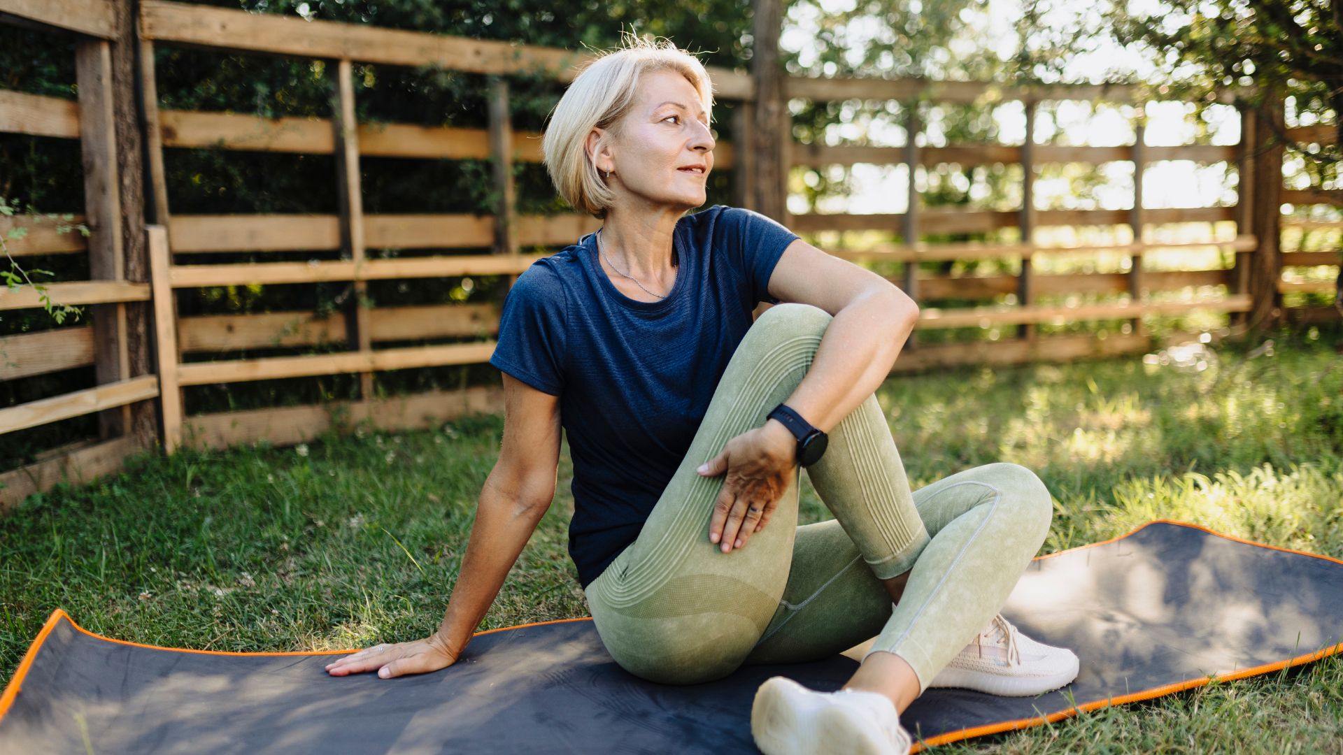Woman doing Pilates exercises on yoga mat in garden