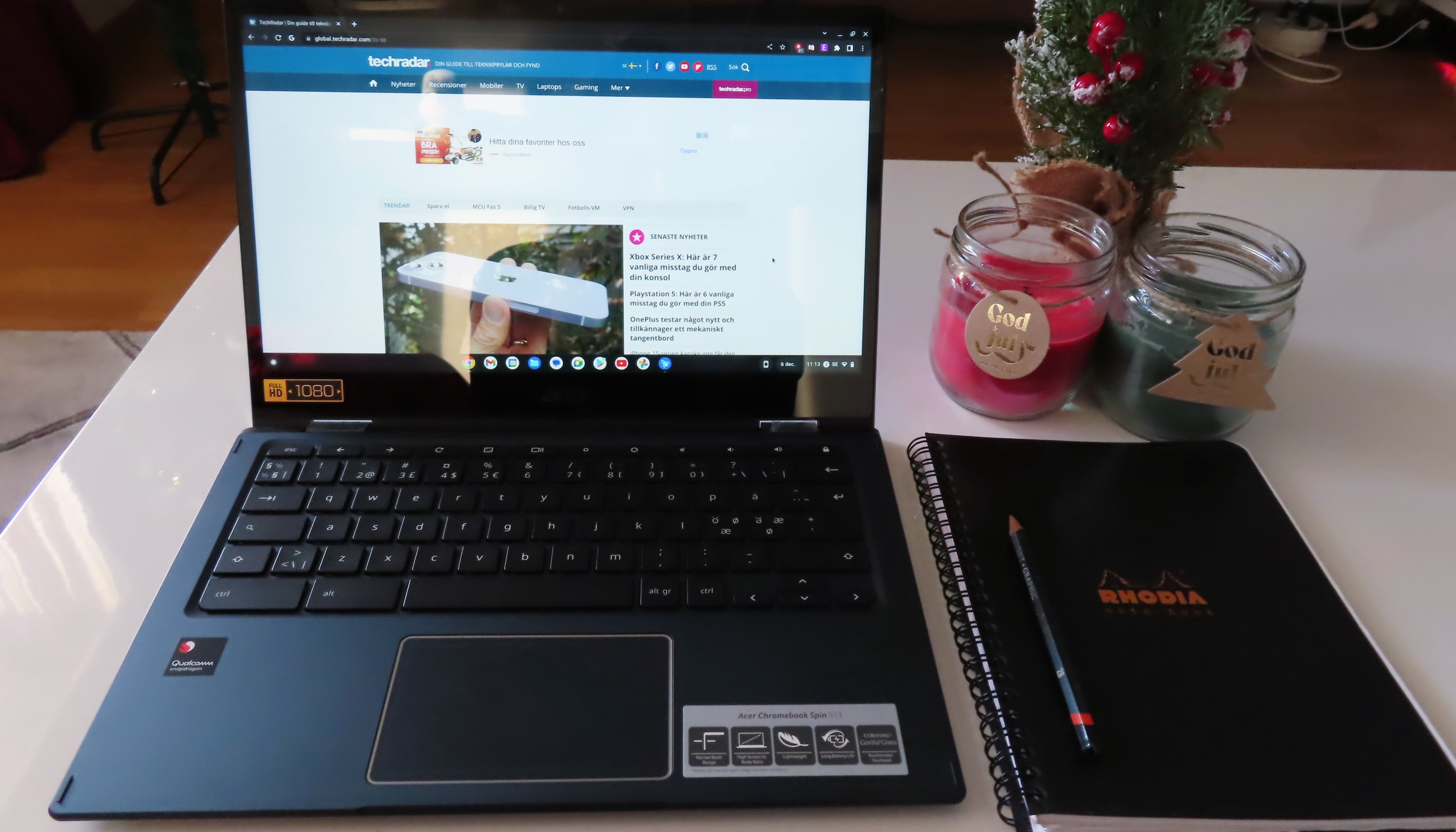 En Acer Spin 513 står öppnad i laptopläge på ett vitt vardagsrumsbord bredvid ett block och ett par ljus.