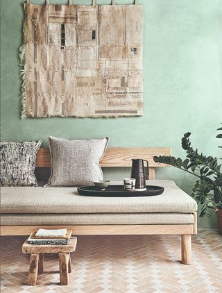 A mint green living room with a statement wall hanging and a beige futon