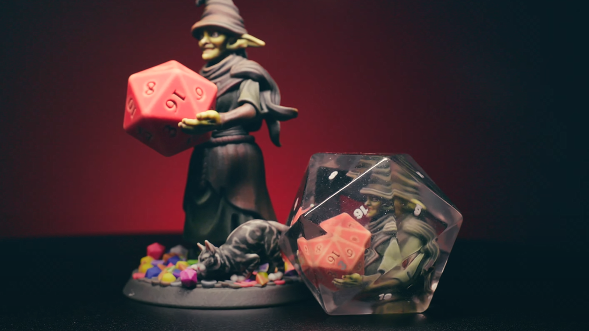 A goblin wizard, holding a dice, and a dice with a goblin wizard holding a dice placed within it.