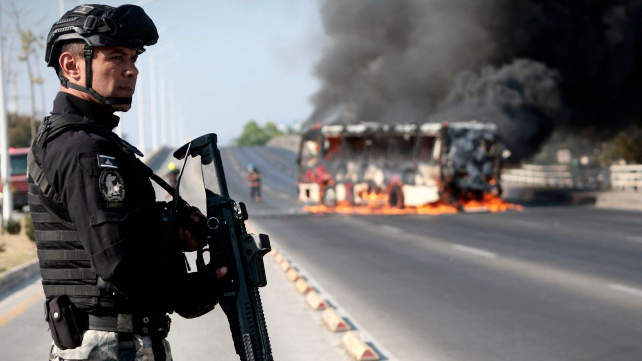 Mexican officer stands guard near burning bus after killing of cartel boss