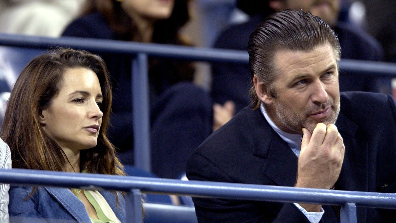 Kristin Davis and Alec Baldwin sitting together at the US Open with serious expressions and blue blazers