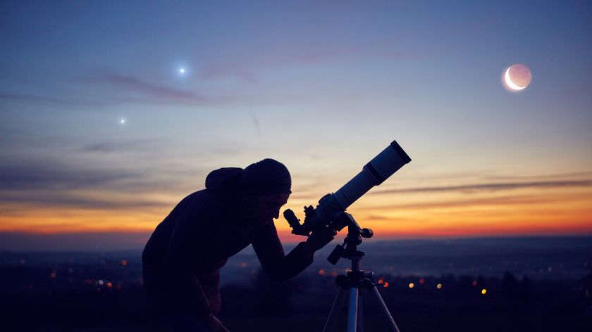 man looks at telescope with planet aligning in the sky alongside the moon.