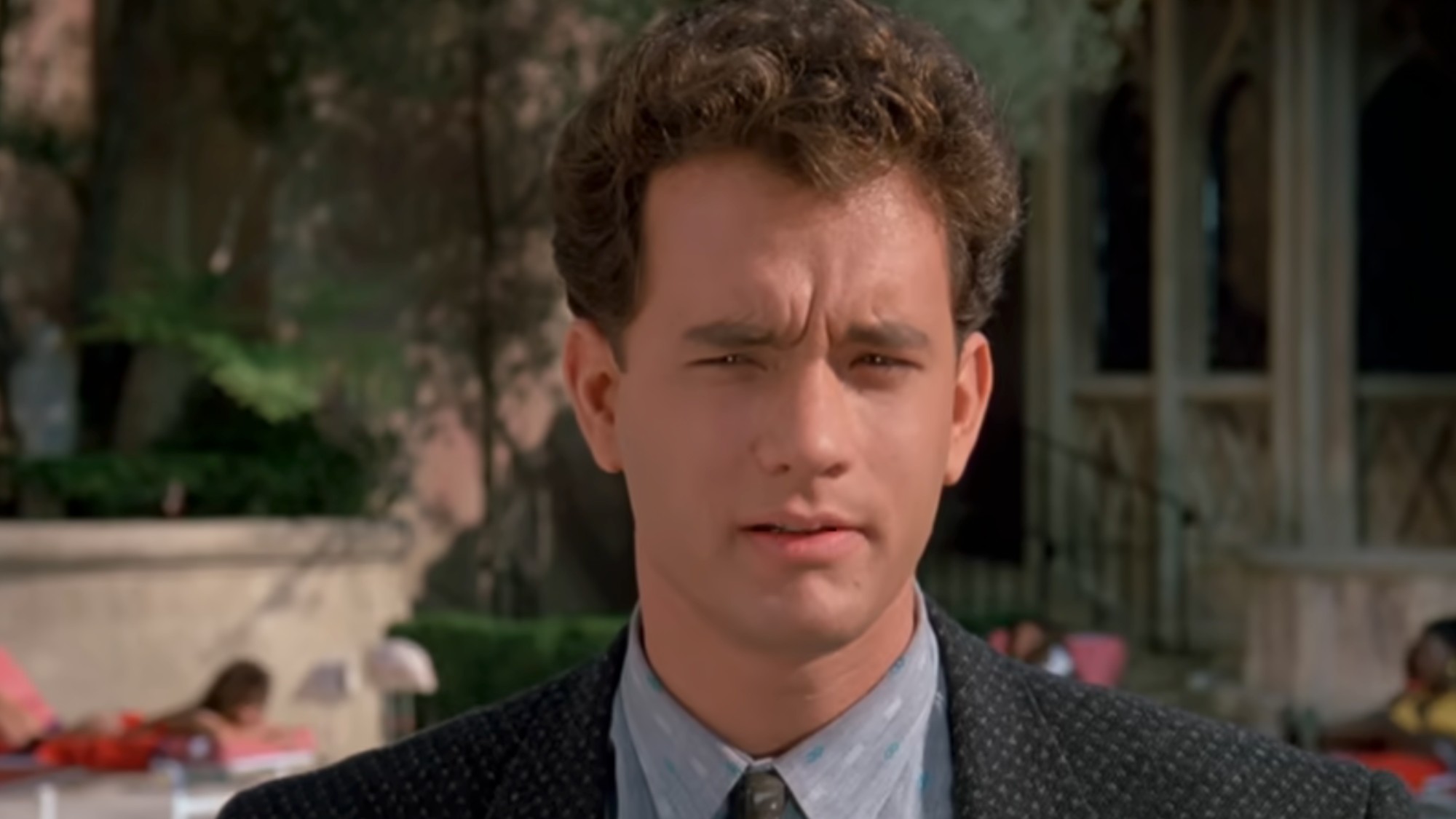 A close up of Tom Hanks wearing a jacket and tie, and looking skeptical in a scene at a mansion in Dragnet