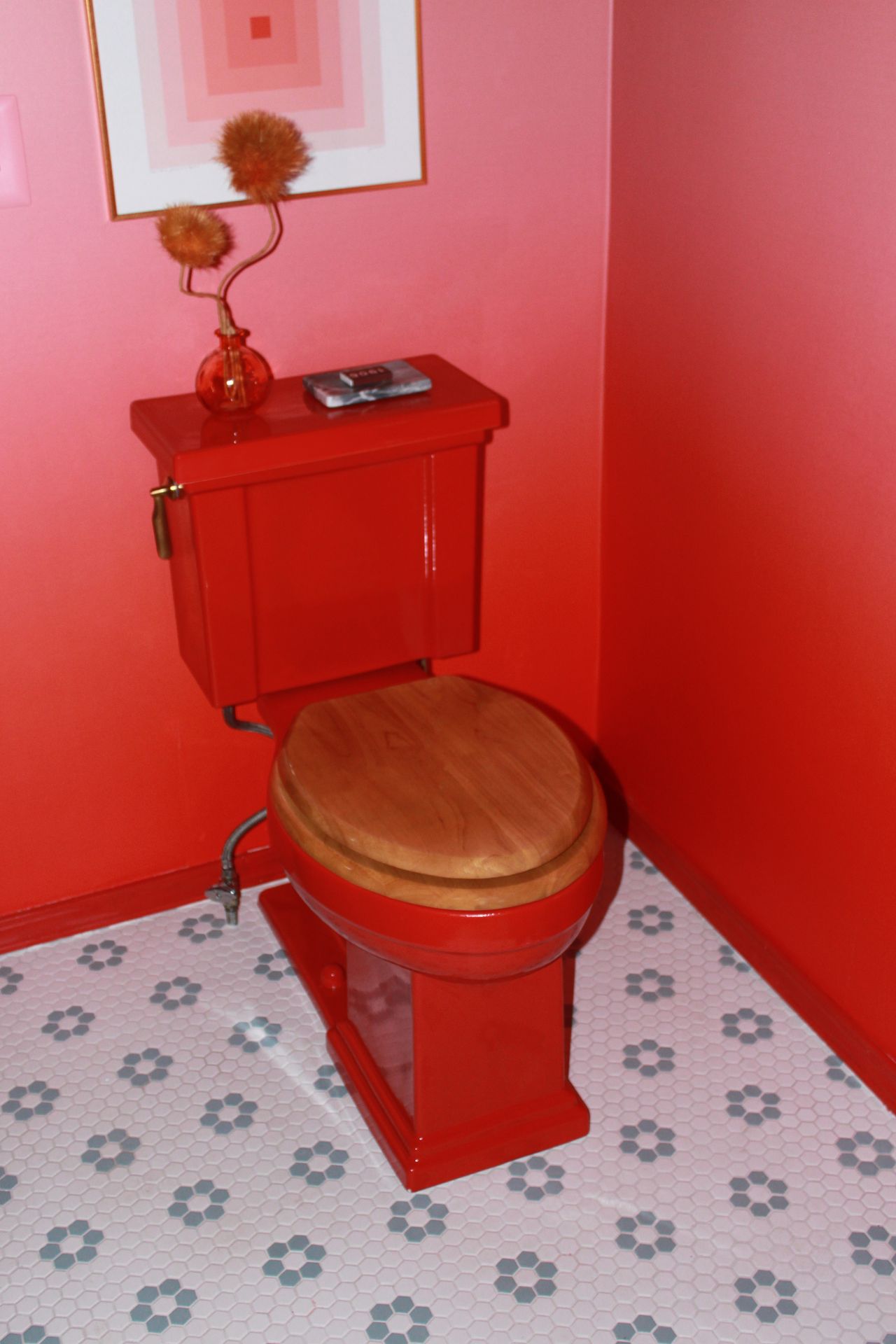 Close-up image of the red toilet in the red and pink ombre bathroom. The body of the toilet is read and the lid is wooden.