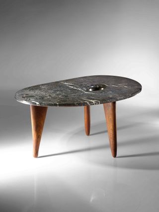 marble top side table with three wooden legs. Photographed against a grey background