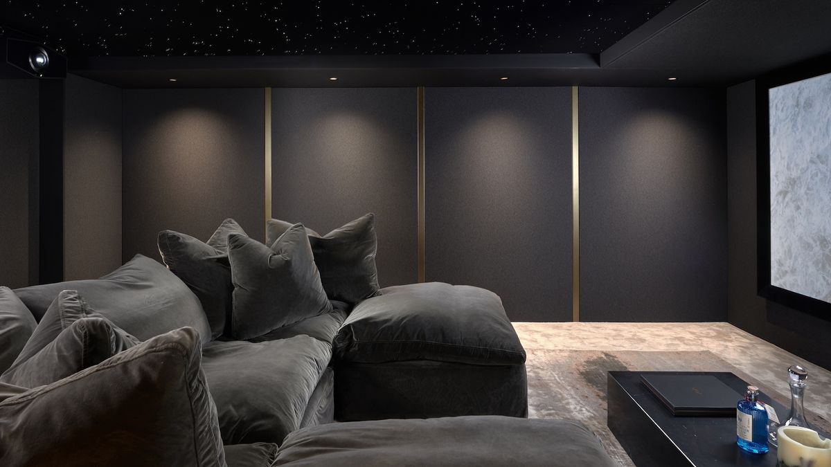 A photograph of a luxury, custom-installed home cinema with a huge projector screen, lush u-shaped sofa, grey walls and lamps