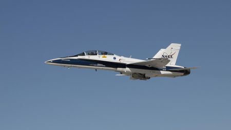 a blue and white fighter jet with the NASA logo flies through open sky