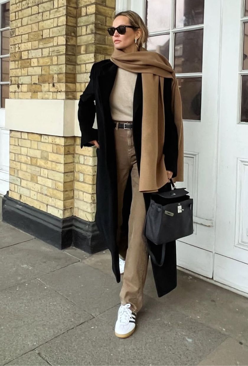 @anoukyve wears camel jeans with a cream jumper, black long coat, camel scarf, white trainers and black bag